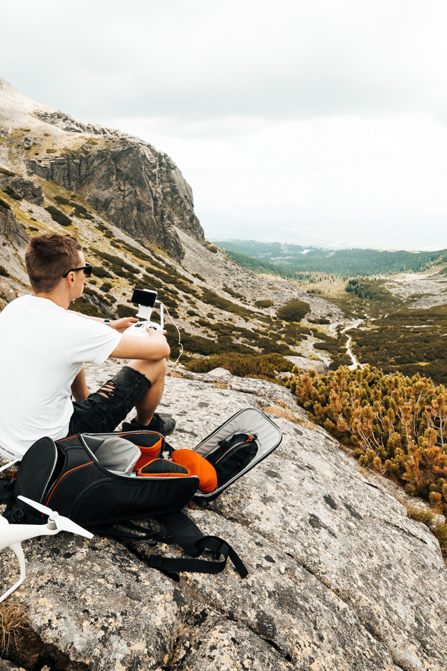 Парень с квадрокоптером сидит на камне в горах 