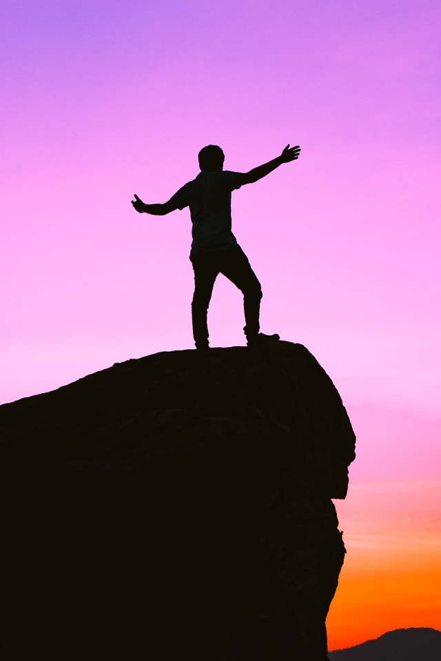 A man stands on the edge of a cliff at sunset