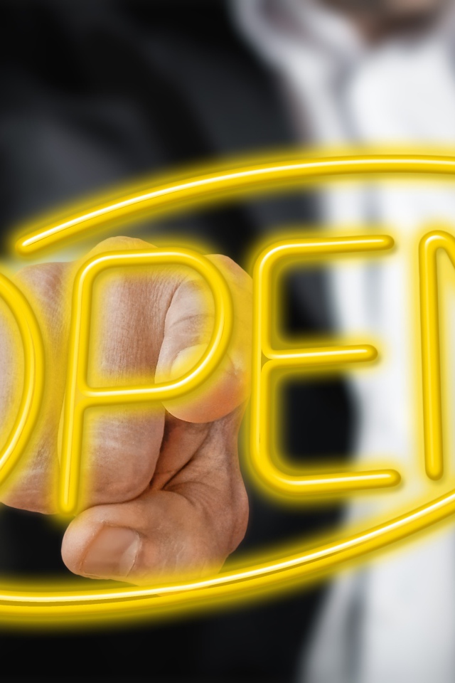 Мужчина трогает пальцем желтую  неоновую  надпись Open 