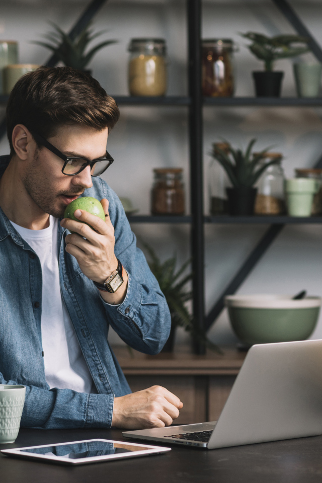 Мужчина с ноутбуком ест яблоко в кафе 