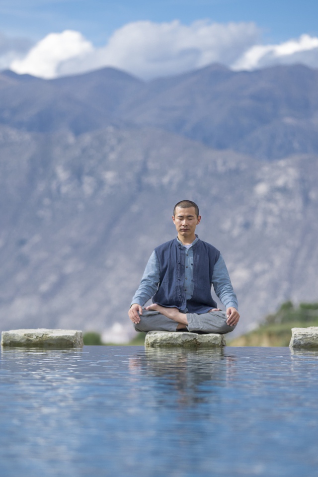 Мужчина азиат в позе лотоса медитирует у воды 