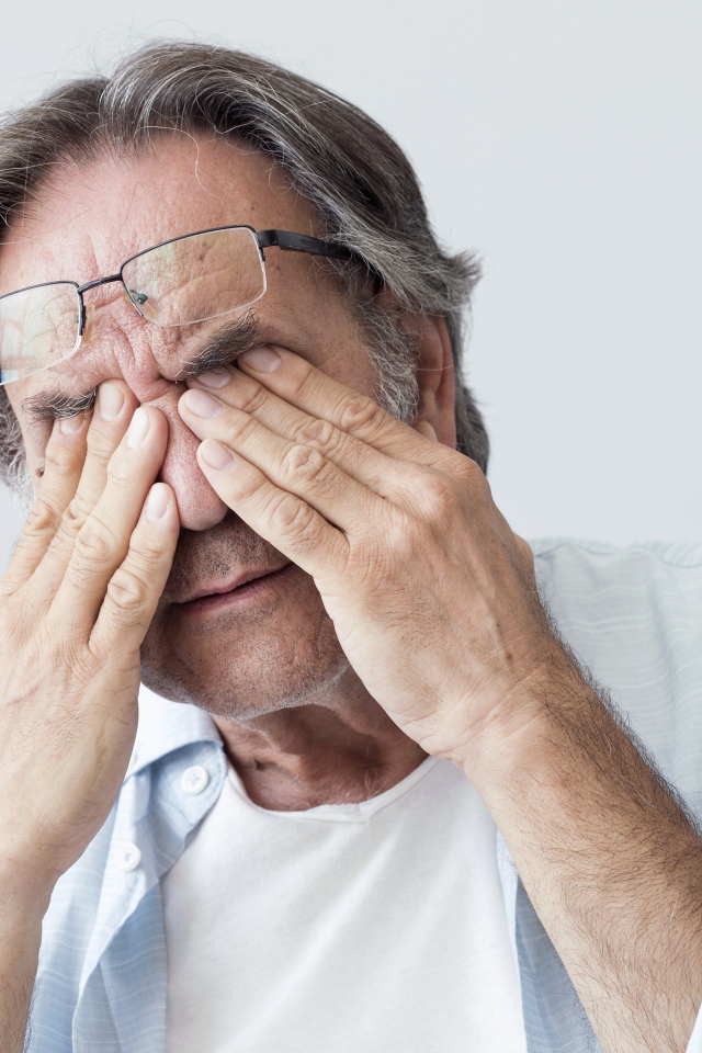 Пожилой мужчина трет глаза на сером фоне