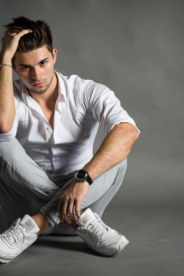 Красивый молодой человек в белой рубашке сидит у стены 