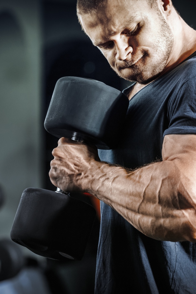 Мужчина бодибилдер в спортзале с гантелей 