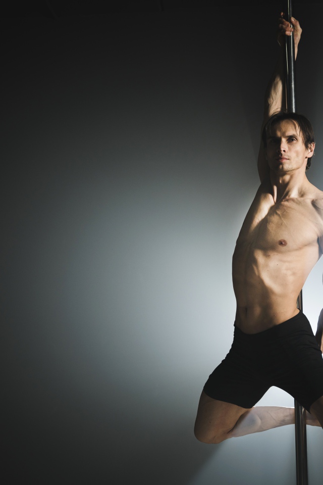 Мужчина танцует на пилоне на сером фоне