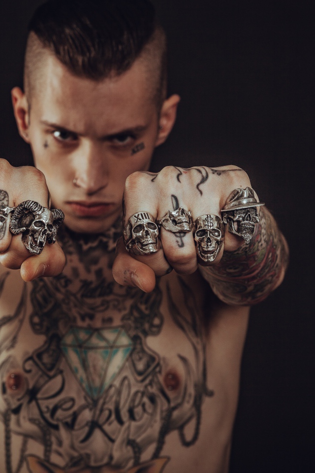 Мужчина с татуировками на теле с перстнями на пальцах