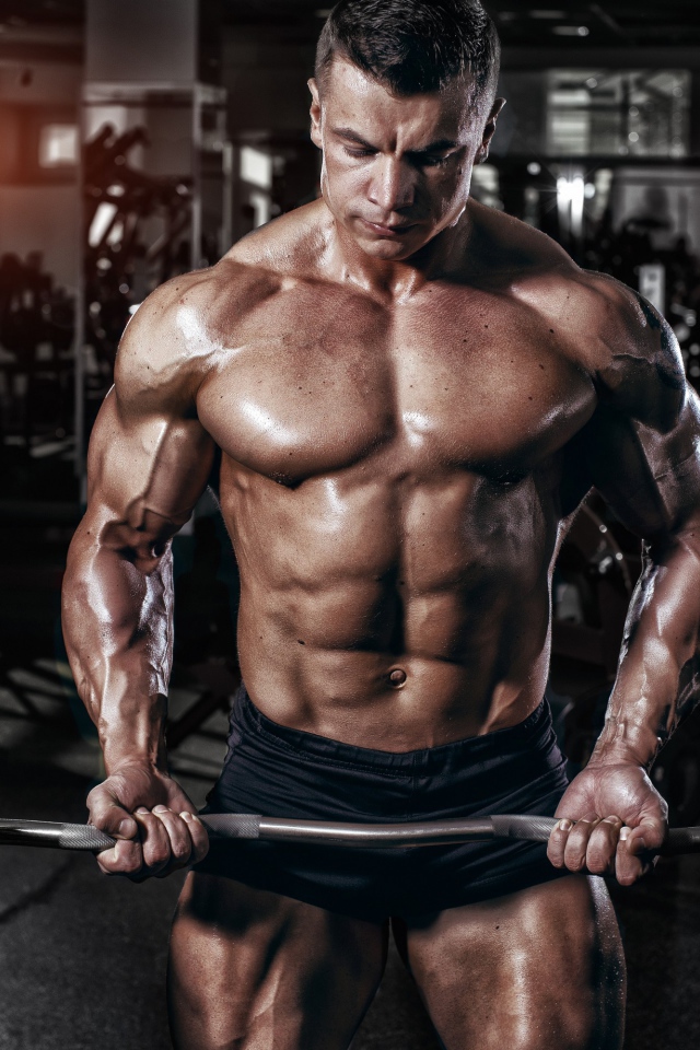 Мускулистый мужчина со штангой в руках в спортзале