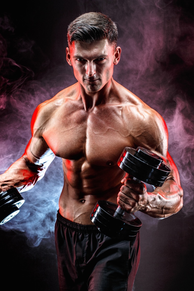 Мускулистый мужчина с гантелями в руках на черном фоне с дымом