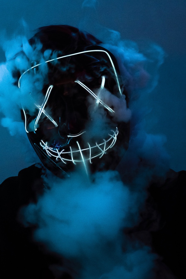 Дым идет из под неоновой маски анонимуса на лице у парня