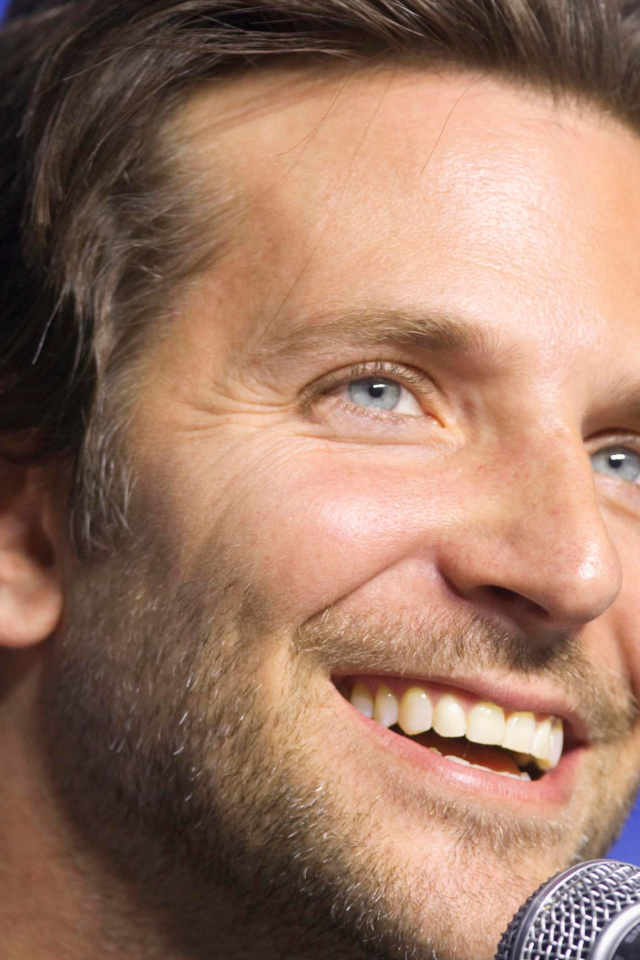 Голубоглазый актер Брэдли Купер с микрофоном на синем фоне