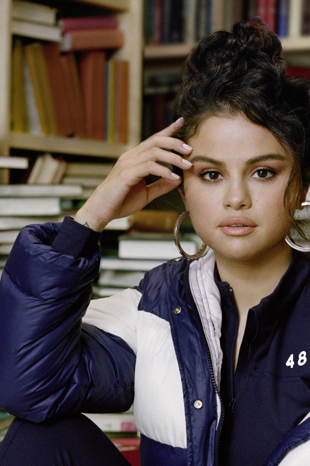 Actress and singer Selena Gomez in a jacket sits in a library