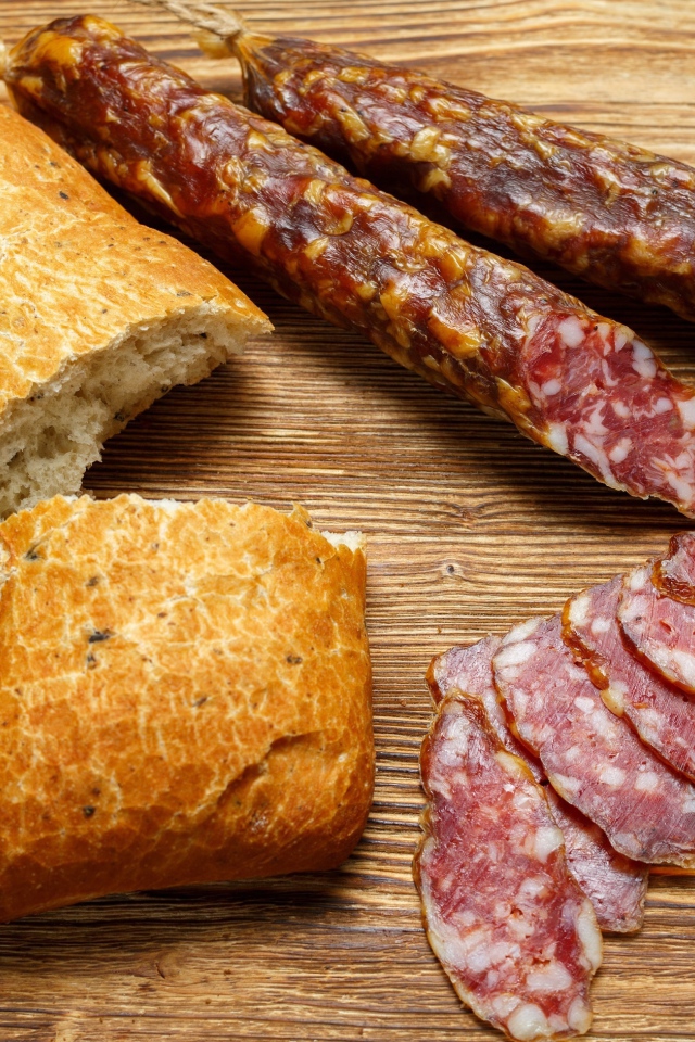 Сухая колбаса на столе с батоном и оливками