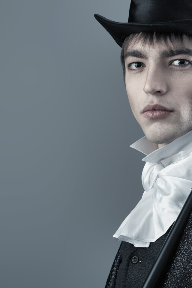 Красивый молодой человек в черном цилиндре и фраке на сером фоне