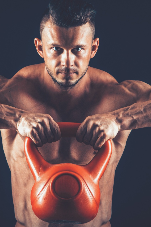 Накаченный парень поднимает тяжелую гирю на черном фоне
