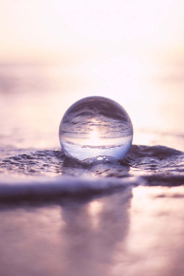 Прозрачный стеклянный шар лежит на пене в море