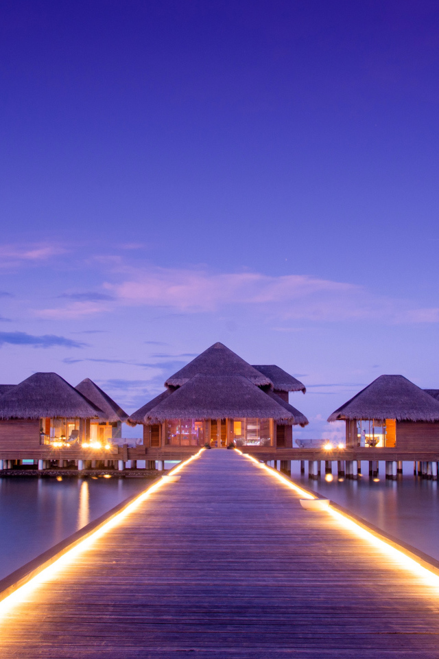 Мост с подсветкой идет к домам на сваях в океане