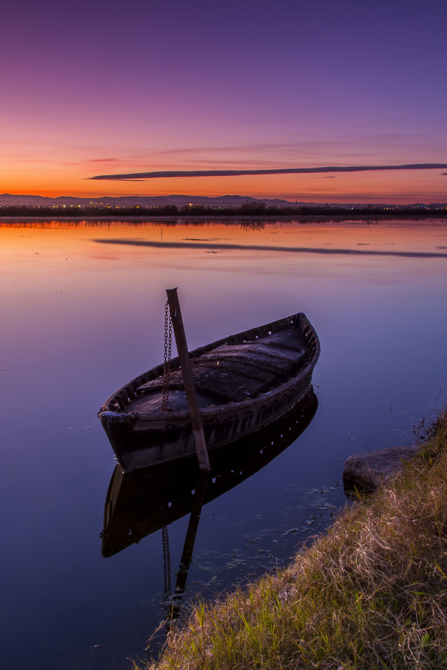 Старая лодка стоит в воде на закате солнца 