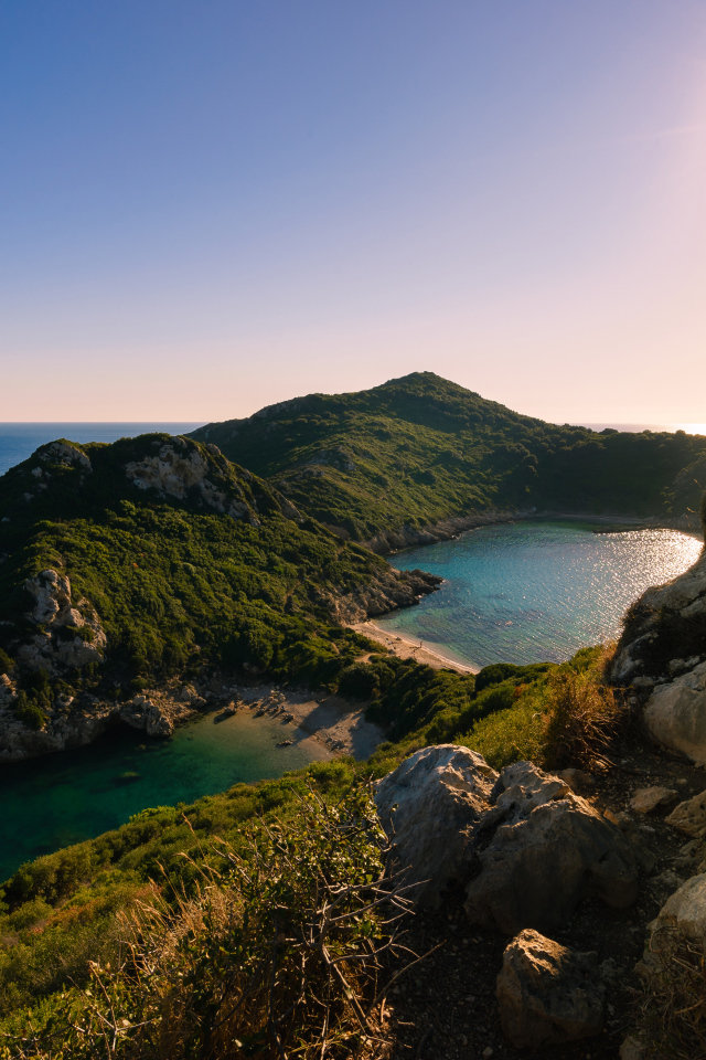Яркое солнце за скалой у тихого моря