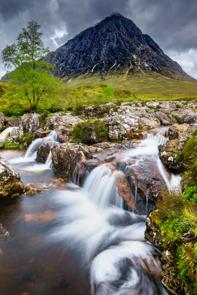 Быстрая вода в реке на фоне высокой горы под грозовым небом 