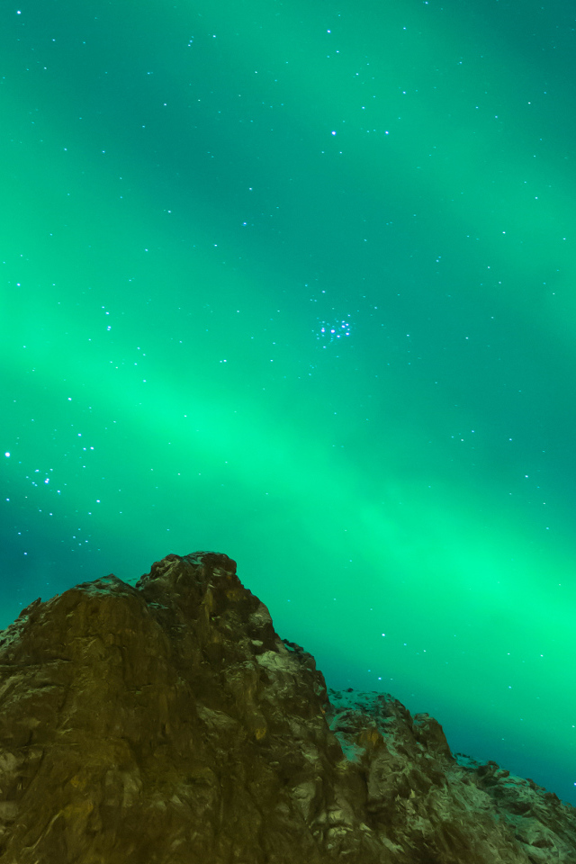 Зеленое северное сияние над верхушкой скалы в небе 