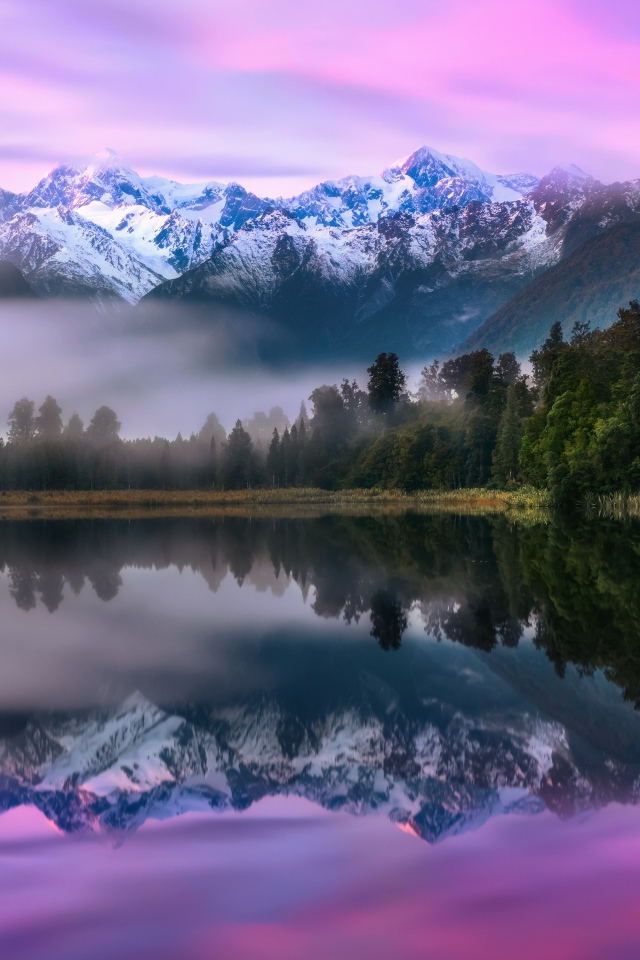 Зеленый лес у туманного озера на фоне гор