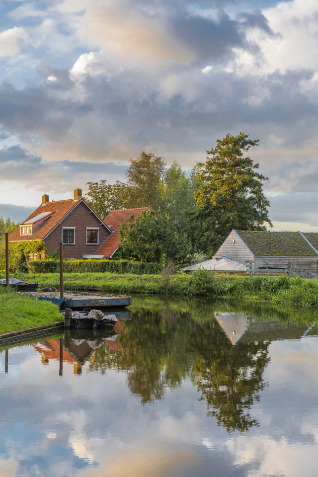 Дома отражаются в реке под небом с белыми облаками