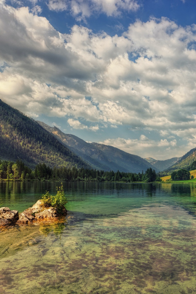 Большие камни в озере на фоне гор под небом с белыми облаками
