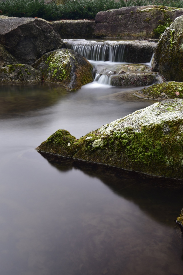 Вода стекает по камням в пруд с большими покрытыми мхом камнями