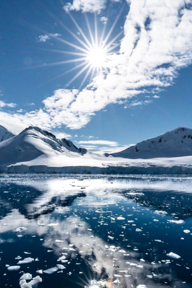 Белые облака в солнечном небе отражаются в озере у заснеженных гор 