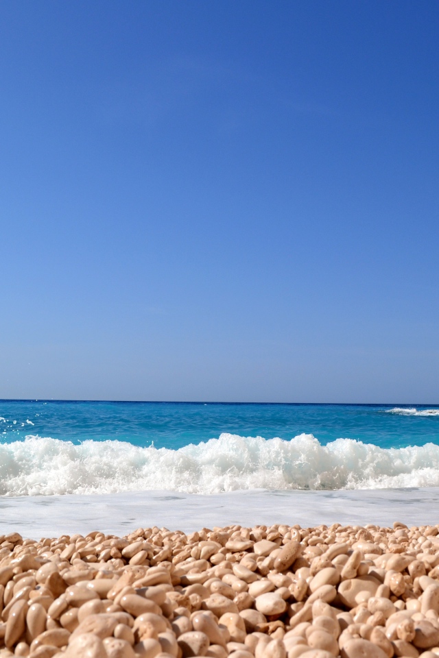 Красивая голубая вода с белыми волнами на пляже с галькой 