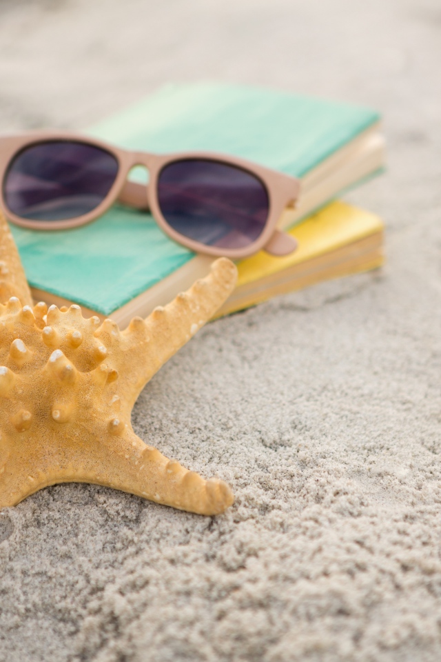 Книги, очки и морская звезда на белом песке 