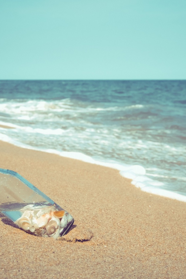 Бутылка с ракушками на песке у моря