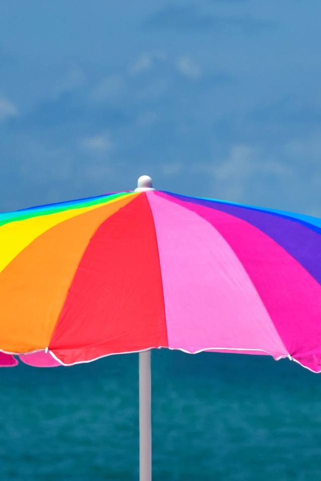 Большой разноцветный пляжный зонт на фоне моря