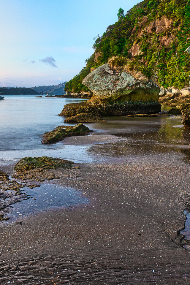 Мокрый песок и большие каменные глыбы на берегу залива