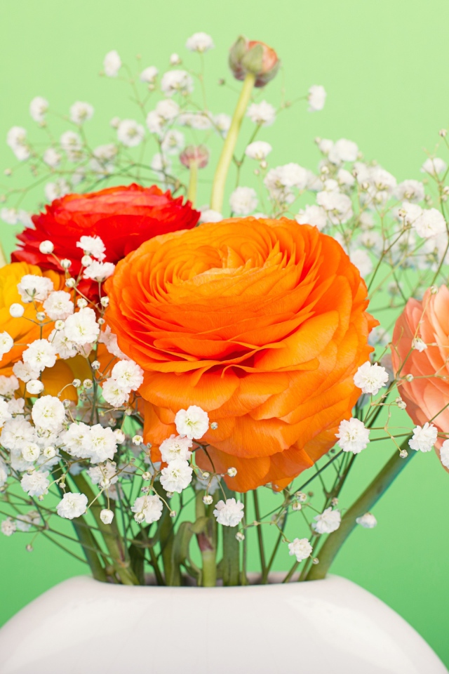 Букет разноцветных лютиков в белыми цветами в вазе на зеленом фоне