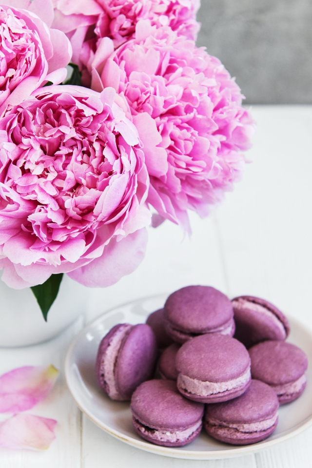Букет розовых пионов на белом столе с десертом макарон 