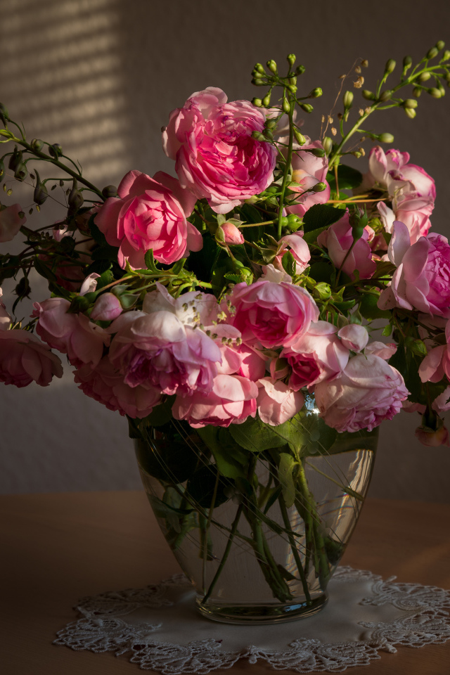 Букет розовых роз в стеклянной вазе не столе в лучах солнца 