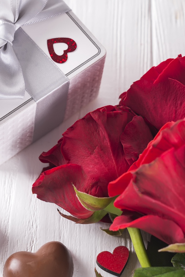 Букет красных роз на столе с конфетами и подарком