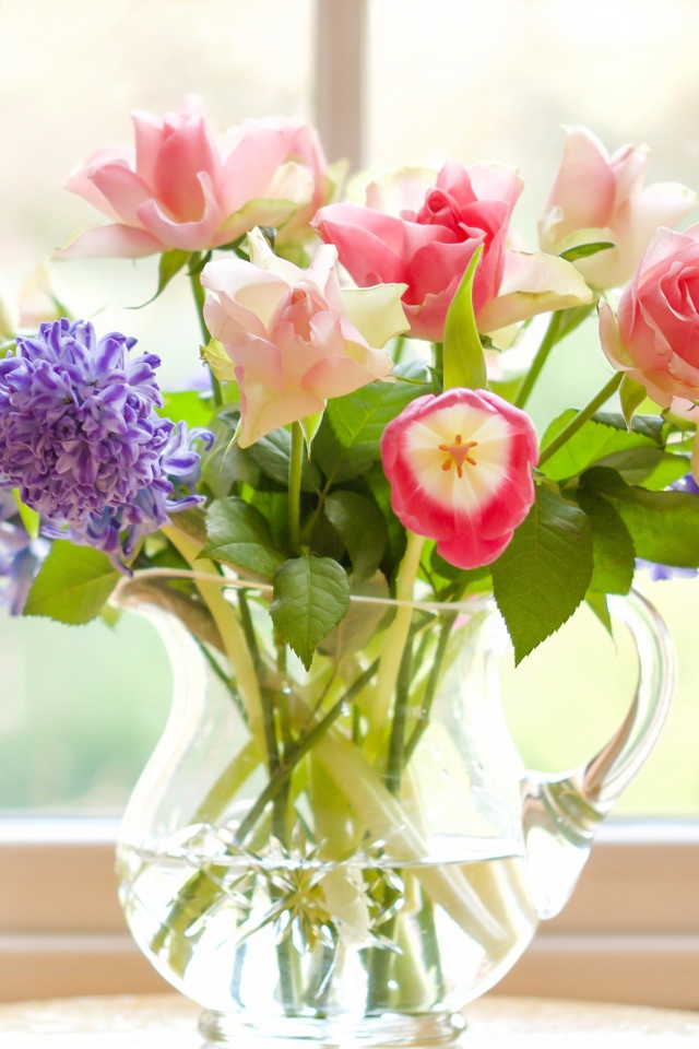 Букет роз, тюльпанов и гиацинтов в стеклянной вазе у окна