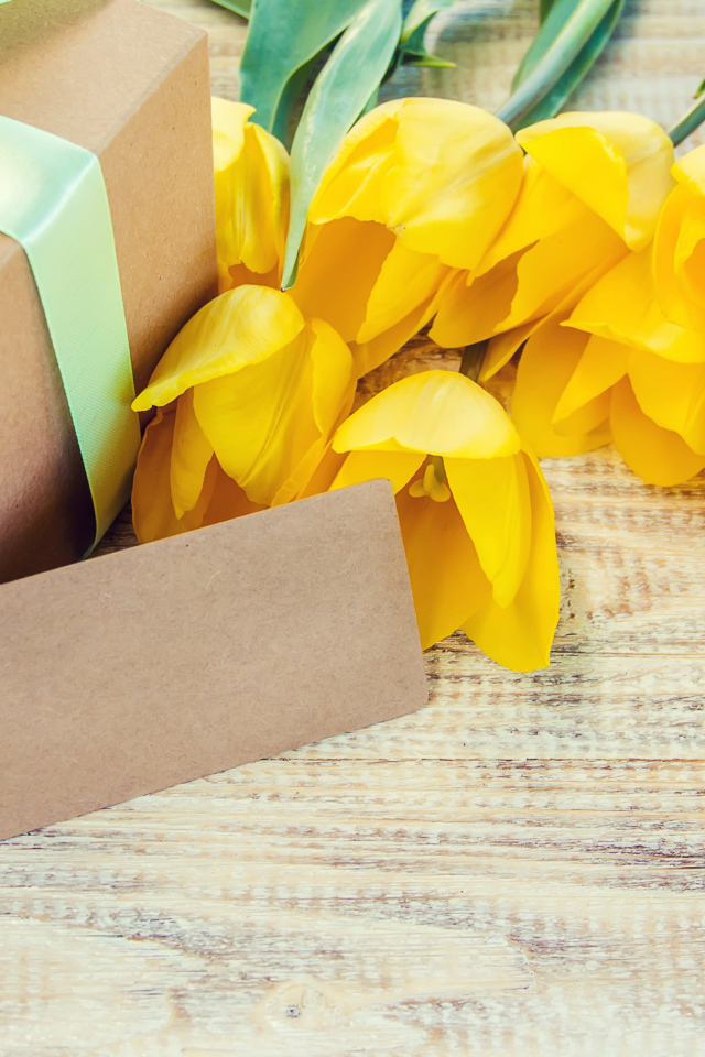 Букет желтых тюльпанов с подарком на столе 