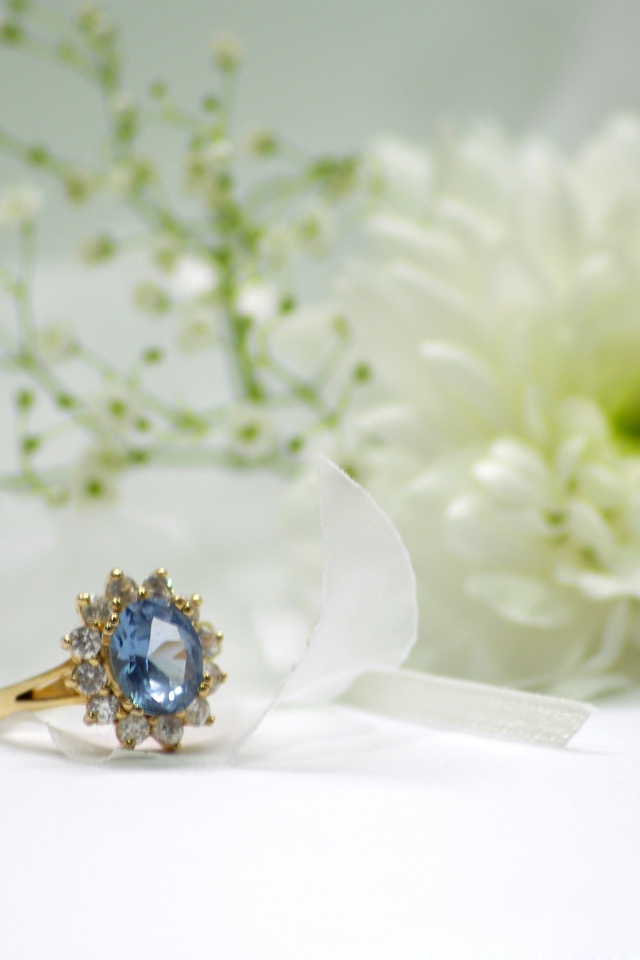 Дорогое кольцо с камнем на столе с белым цветком