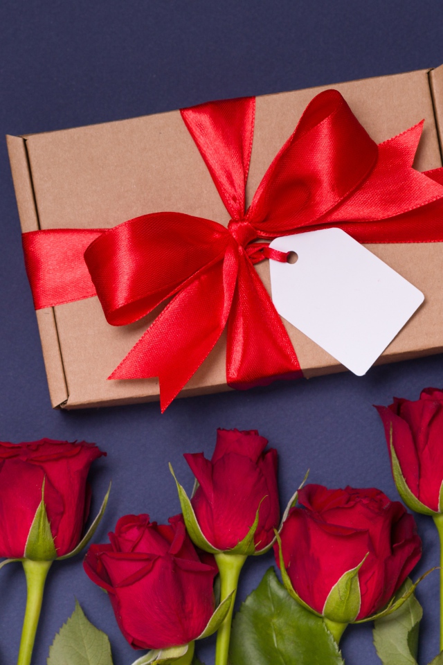 Подарок с красным бантом на столе с розами