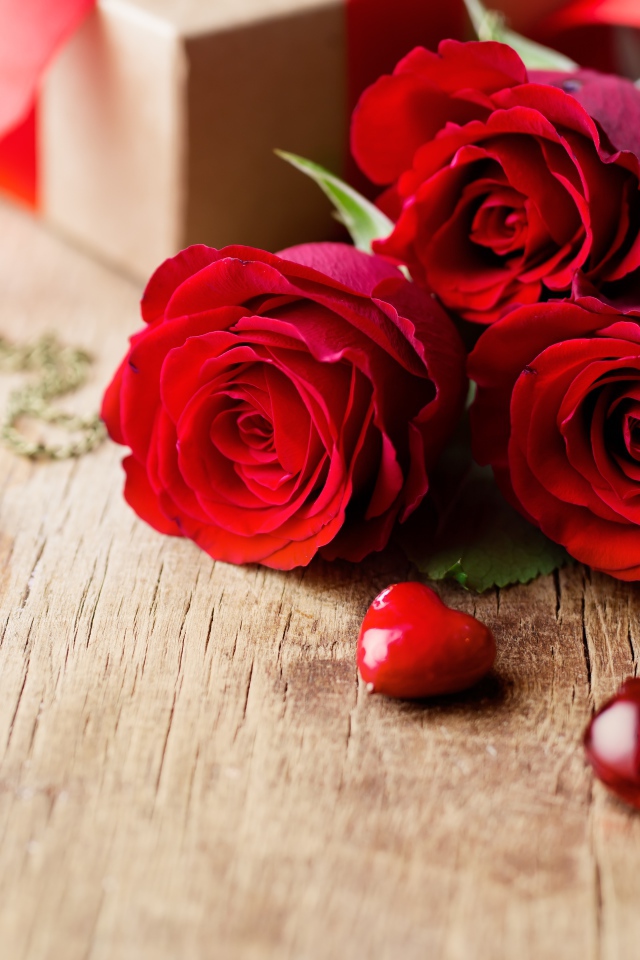 Три красивые красные розы на столе с сердечками и ключами