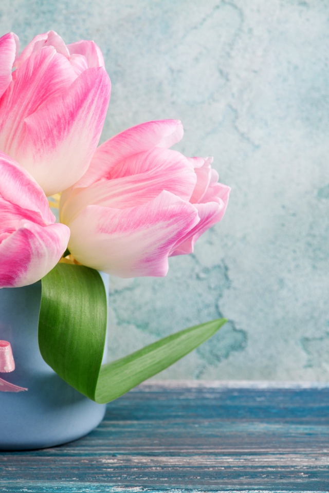 Три розовых тюльпана в чашке на столе 