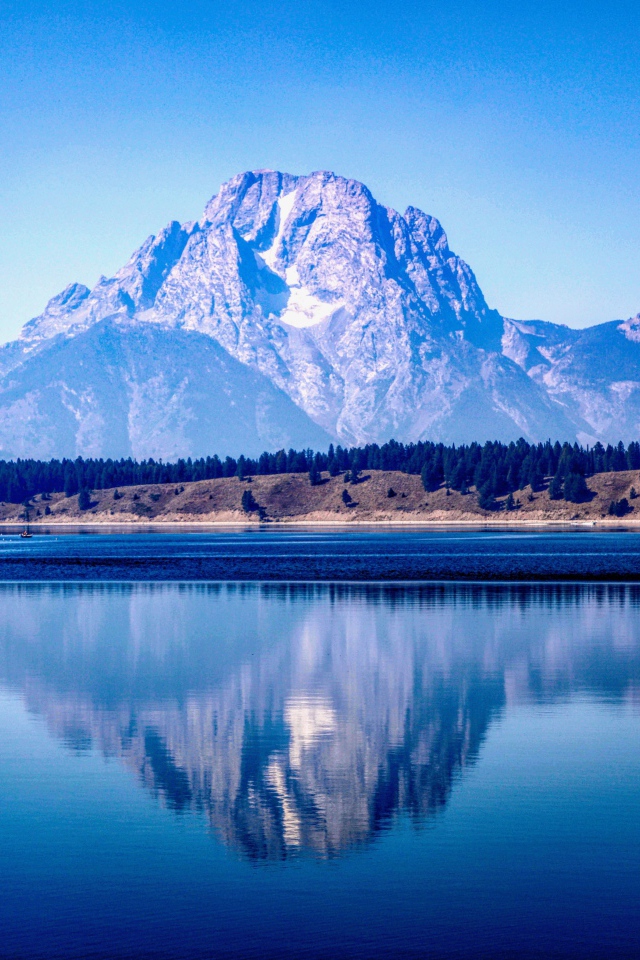 High mountains are reflected in a lake under a blue sky