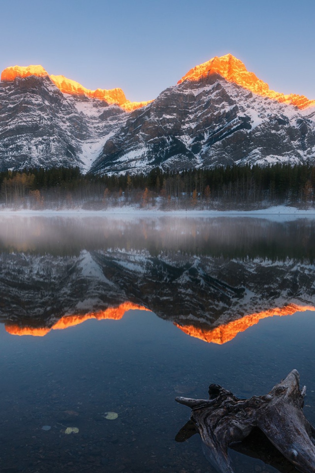 Вершины гор в лучах солнца отражаются в чистой воде озера