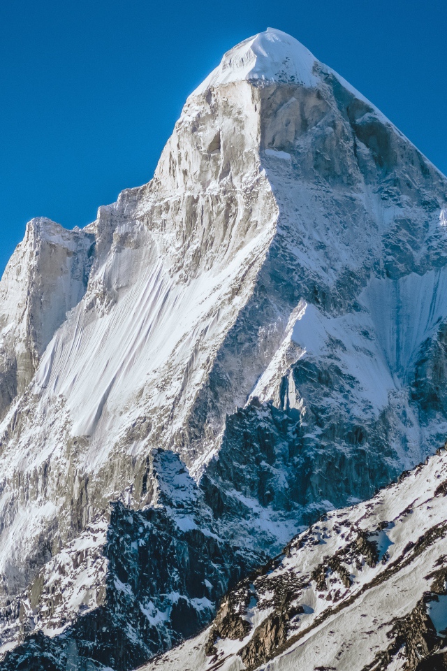 Острая вершина заснеженной горы под голубым небом