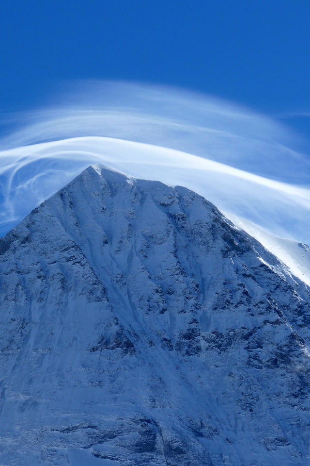Белое облако в голубом небе над заснеженной горной вершиной