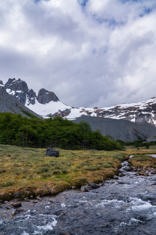 Быстрая река у заснеженных гор под густыми белыми облаками