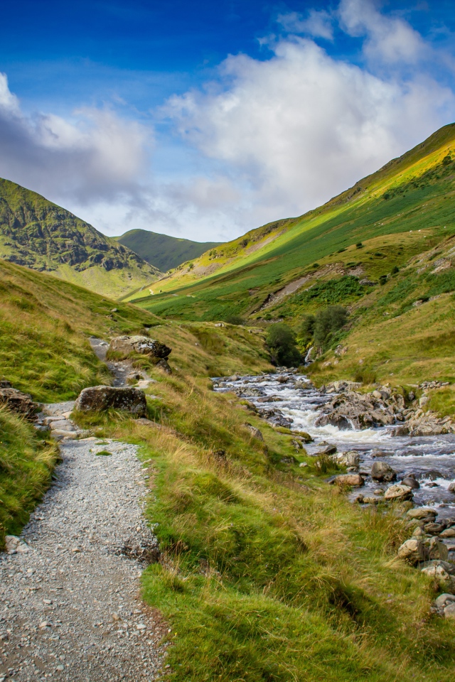 Тропа у реки на фоне покрытых зеленью гор 